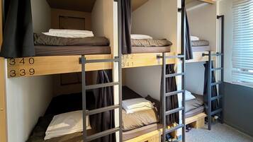 A dormitory room with bunk beds, numbered beds, and a window with blinds.