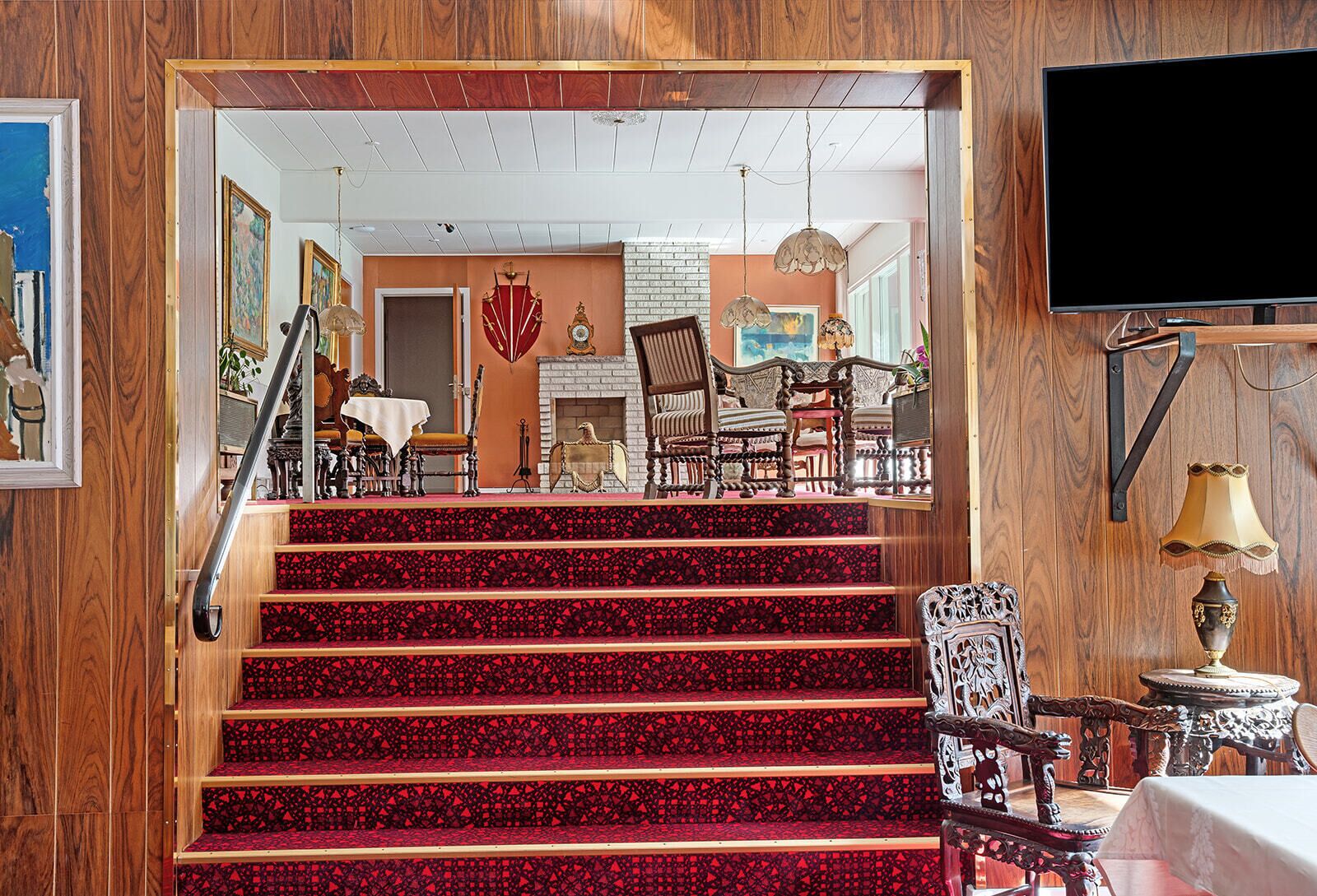 A staircase with red carpet leading to a dining area with wooden furniture and a fireplace.