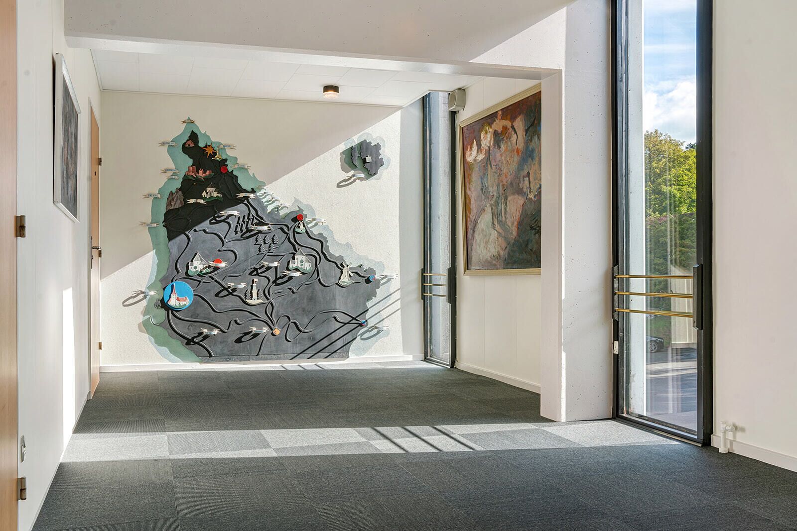 Ein Flur mit einem großen, abstrakten Wandgemälde, einer Glastür, die nach draußen führt, und einem Gemälde an der Wand.