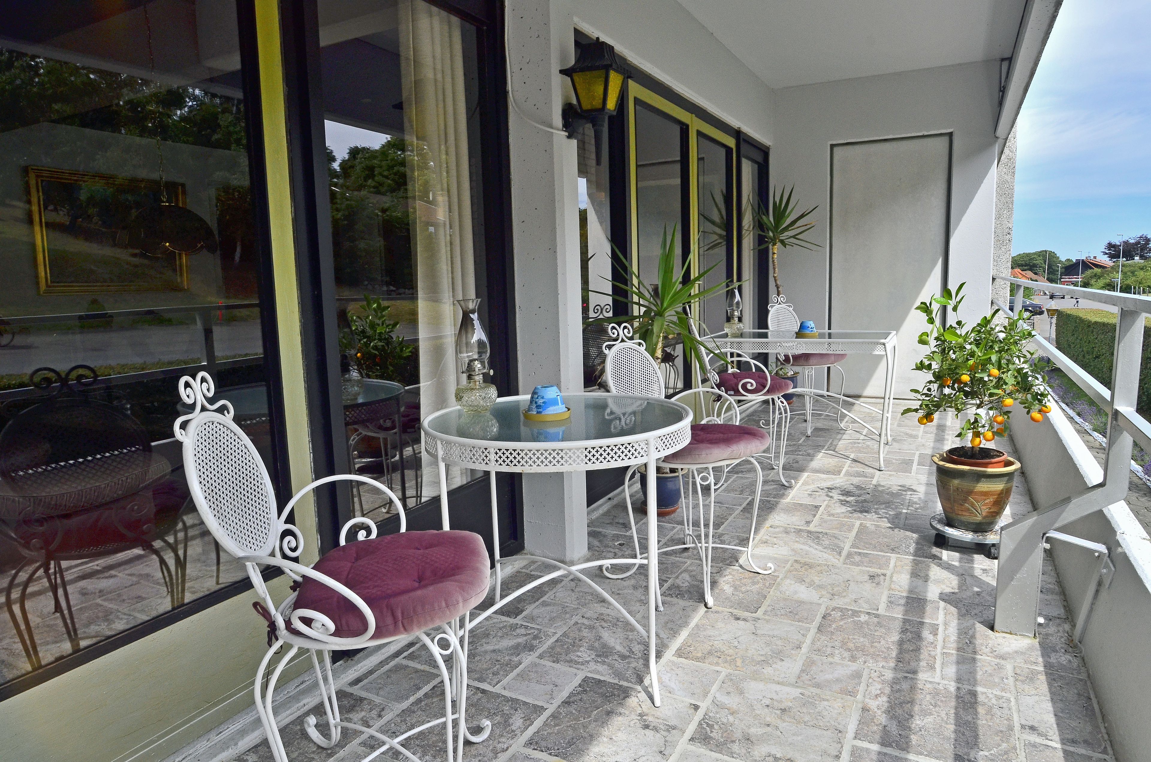 A balcony with a round table and chairs, potted plants, and a view of the surrounding area.