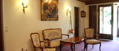 Um quarto com uma mesa de madeira e quatro cadeiras estofadas, um quadro na parede e duas luminárias fixadas na parede.
