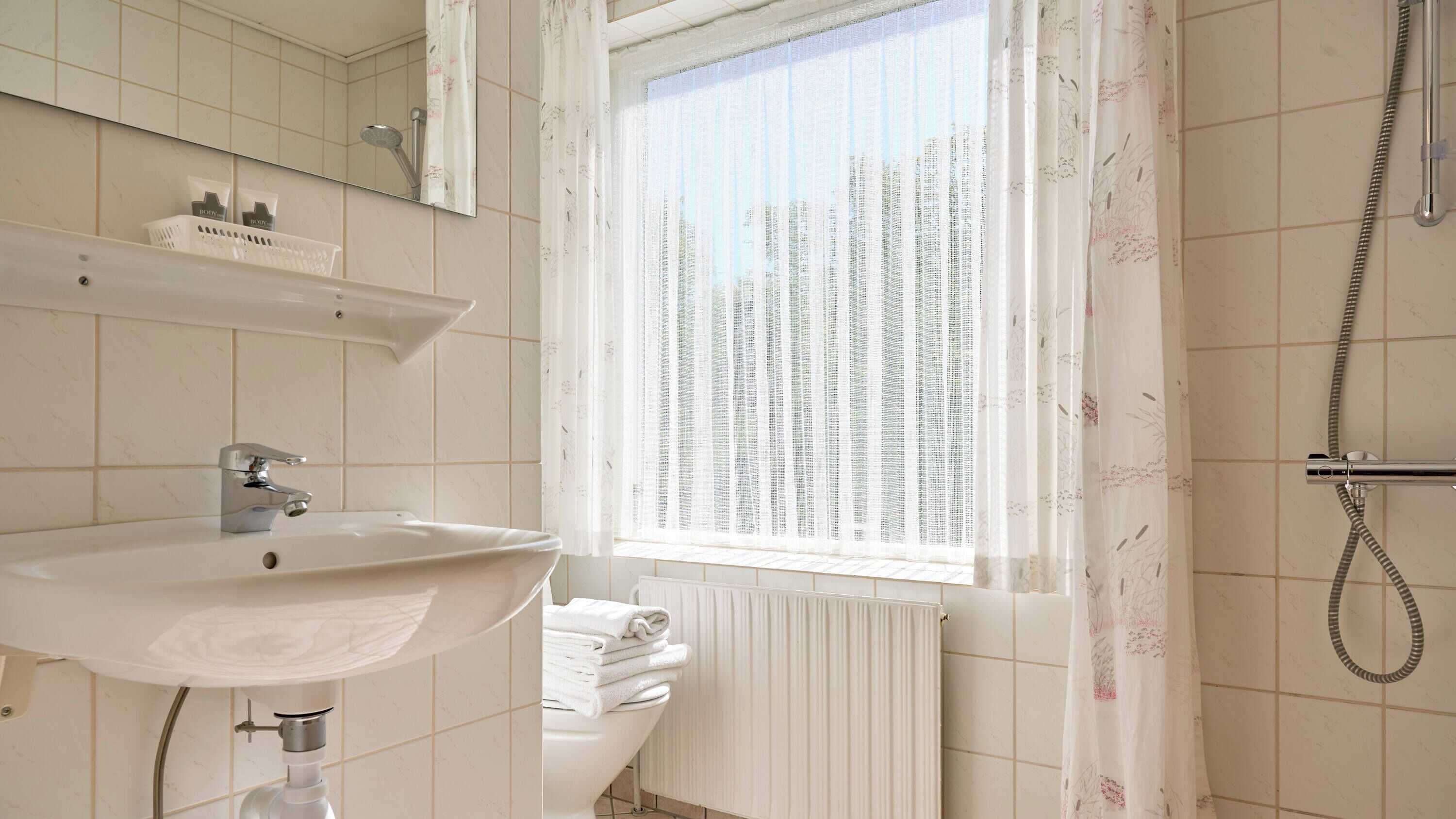 A bathroom with a sink, mirror, shower, and radiator.