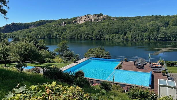 A swimming pool with a view of a lake and forested hills. - Hotel Hammersø - Adults Only (Allinge)