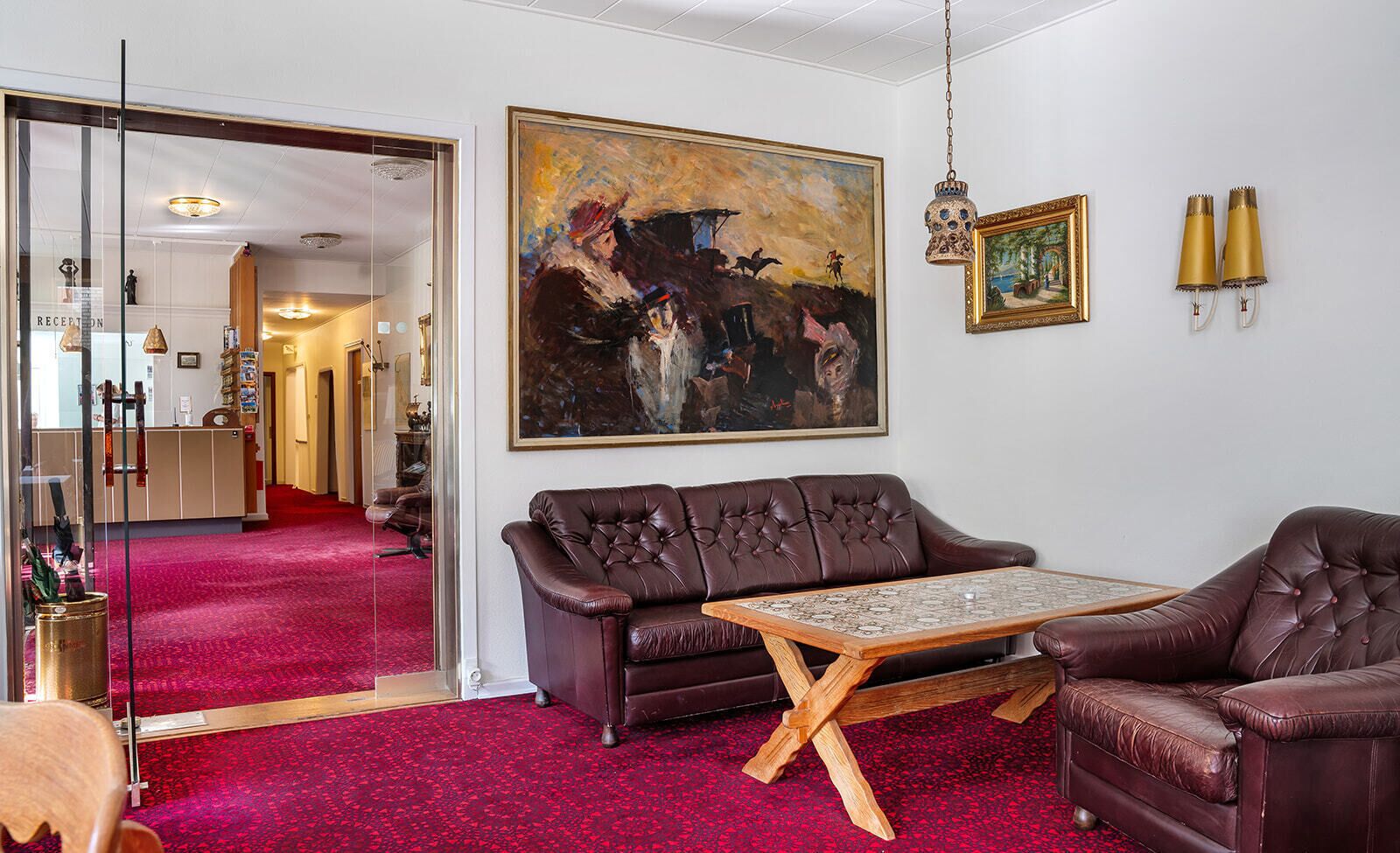 Un salon avec une moquette rouge, un canapé en cuir marron, une table basse et un tableau accroché au mur.