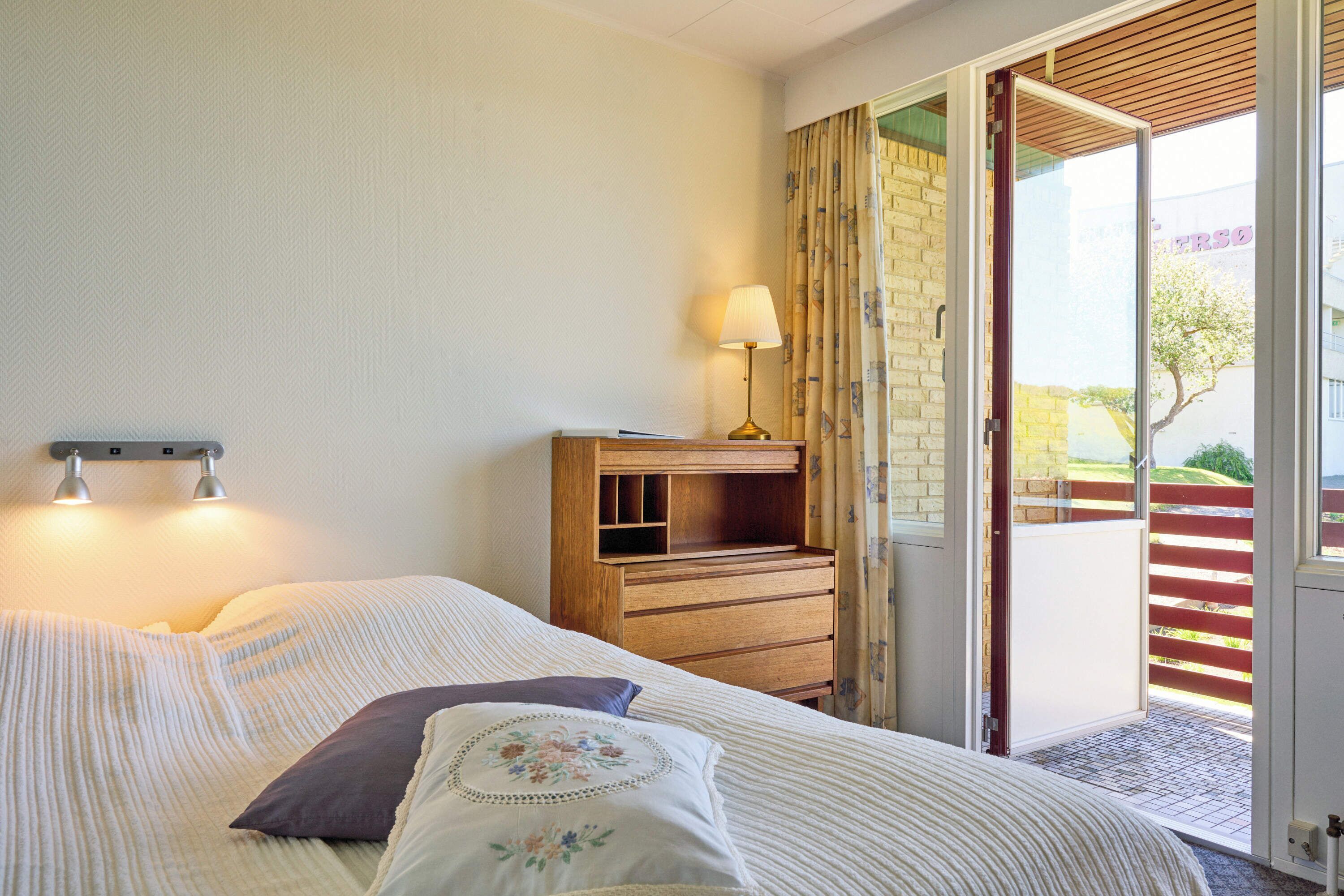 A bedroom with a bed, a nightstand, a lamp, and a sliding glass door leading to an outdoor area.
