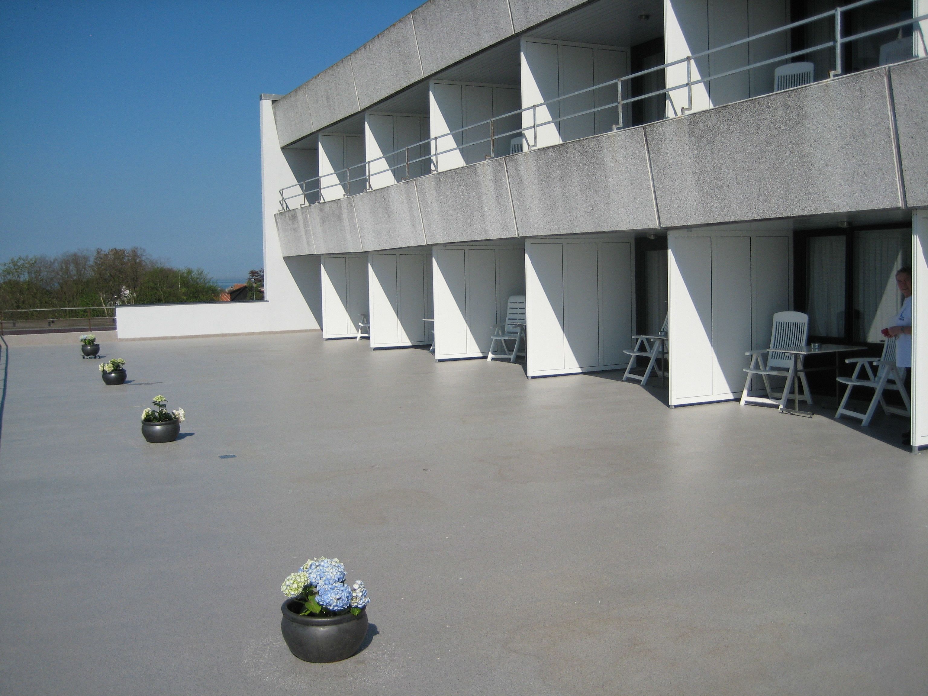 A modern building with a flat roof, multiple balconies, and outdoor seating areas.