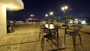 Un patio al aire libre con una mesa y sillas, farolas y vistas a la ciudad iluminada de noche.