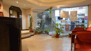 Un hall de hotel con mostrador de recepción, plantas en macetas, una escalera y una zona de estar.