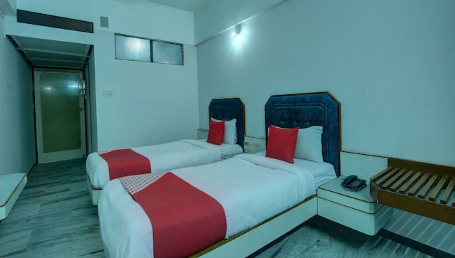 Habitación de hotel con dos camas, una mesita de noche, un teléfono y una puerta.