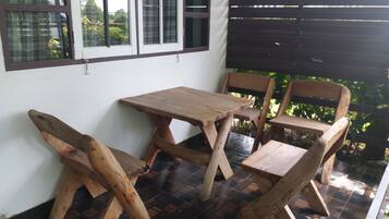 A wooden table and chairs set on a tiled patio with a view of greenery.