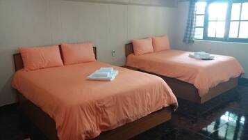 Two beds with matching orange bedding and pillows, a white bedside table, and a window with a curtain.