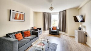 Ein modernes Wohnzimmer mit einer Couch, Sesseln, einem Couchtisch, einem Fernseher und einem Schrank.