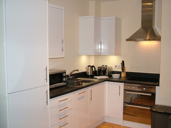 A modern kitchen with white cabinets, a stainless steel range hood, a microwave, a toaster, and a sink. - Stratford Apartment (Newmarket)