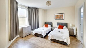 Ein Hotelzimmer mit zwei Betten, einem Fenster mit Vorhängen, einem Heizkörper und einem gerahmten Bild an der Wand.