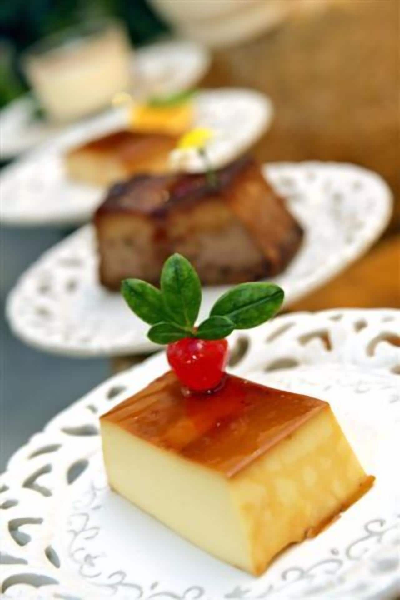 Un postre con una baya roja encima, servido en un plato blanco con un borde decorativo.