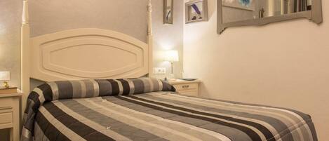 A neatly made bed with a striped bedspread and a matching pillow, a bedside table with a lamp, and a wall-mounted mirror.