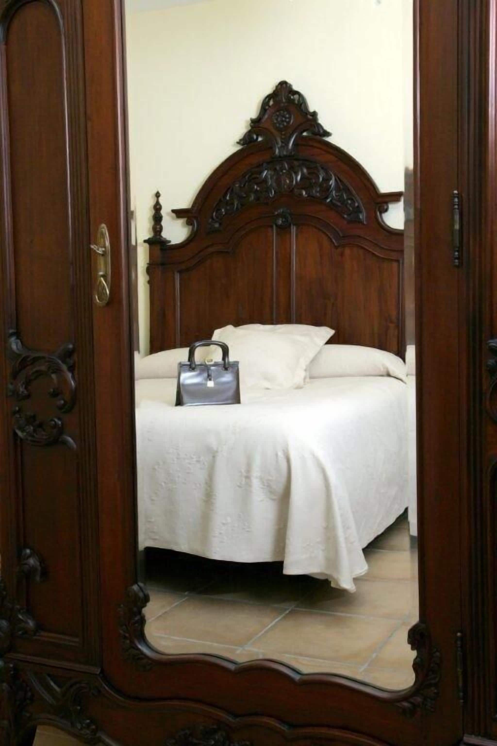 Un dormitorio con cabecera de cama de madera, una colcha blanca y un bolso gris sobre la cama.