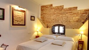 A bedroom with a brick ceiling, two beds, two bedside tables with lamps, and a window with a view of a building. - Hotel La Posada del Infante (La Puebla de los Infantes)