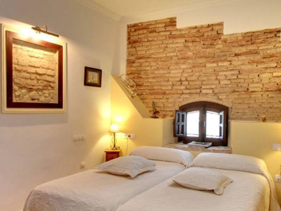 Un dormitori amb sostre de rajola, dos llits, dues taules de nit amb làmpades i una finestra amb vista a un edifici.