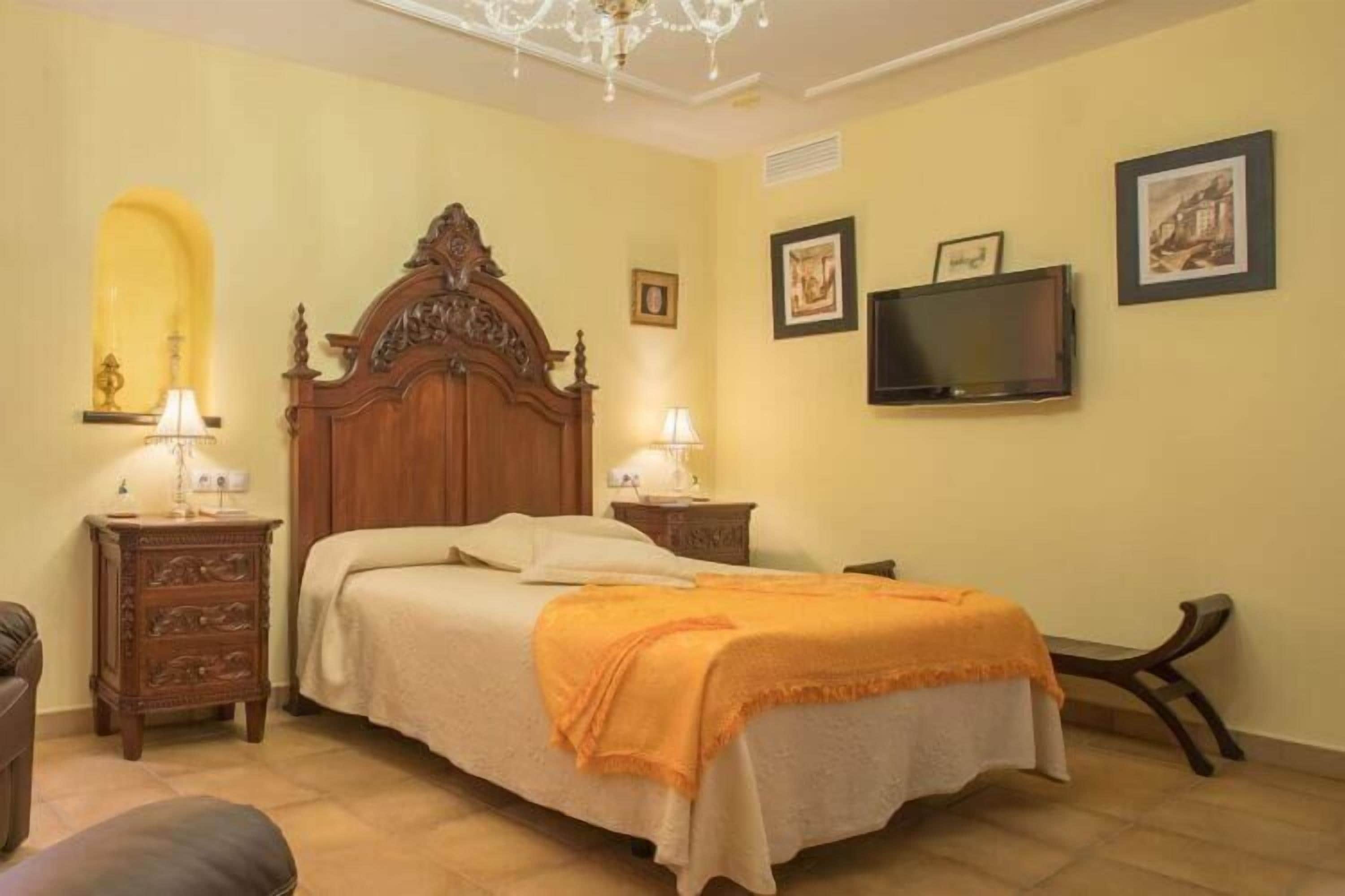 Un dormitorio con una cama de madera, dos mesitas de noche con lámparas, un televisor en la pared y cuadros enmarcados.