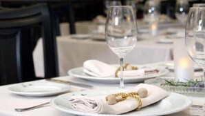 A dining table set with white plates, glasses, and napkins, with a dark wooden cabinet in the background. - Hotel La Posada del Infante (La Puebla de los Infantes)