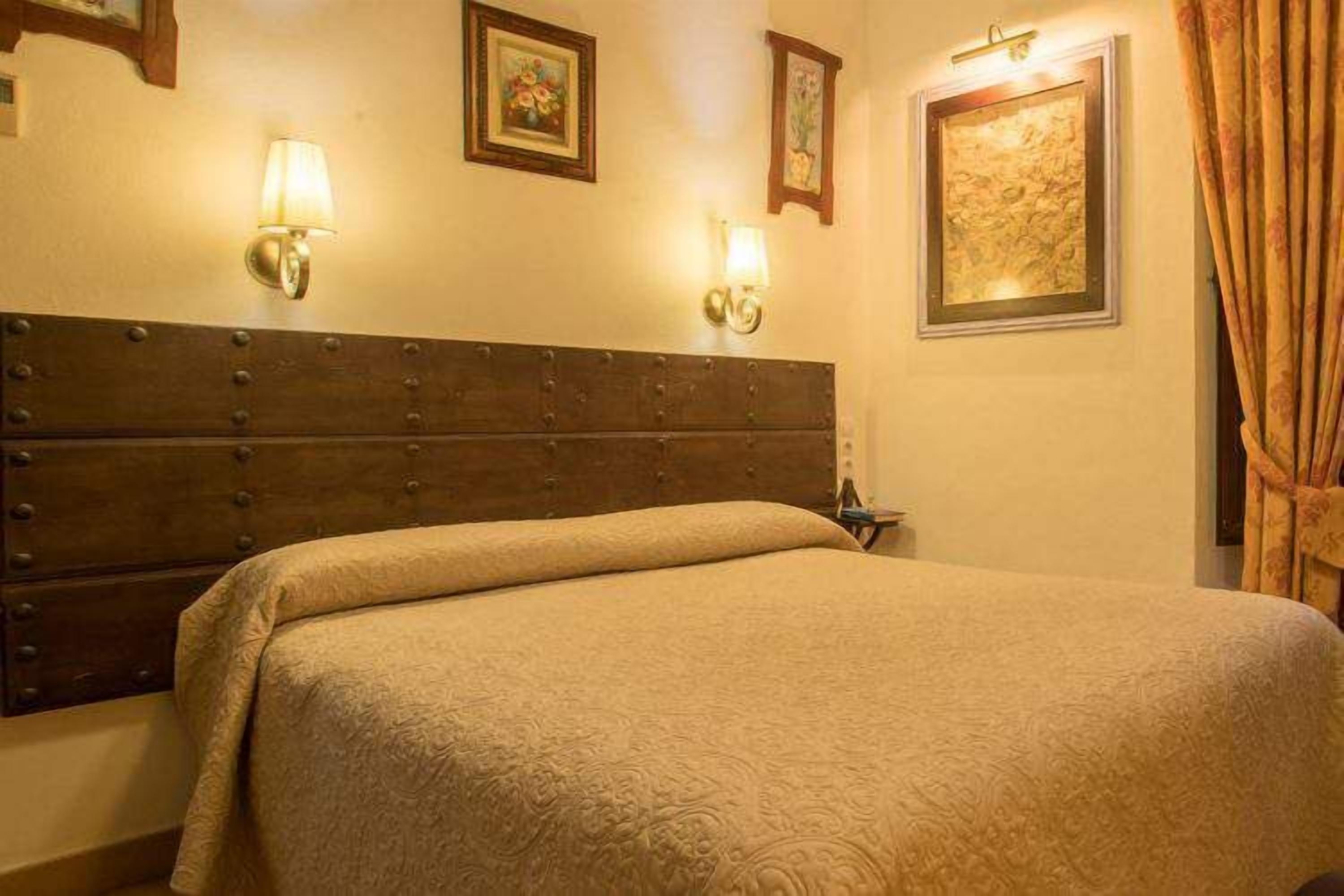 Habitación de hotel con una cama grande, cabecera de madera, dos lámparas de pared y obras de arte enmarcadas en las paredes.