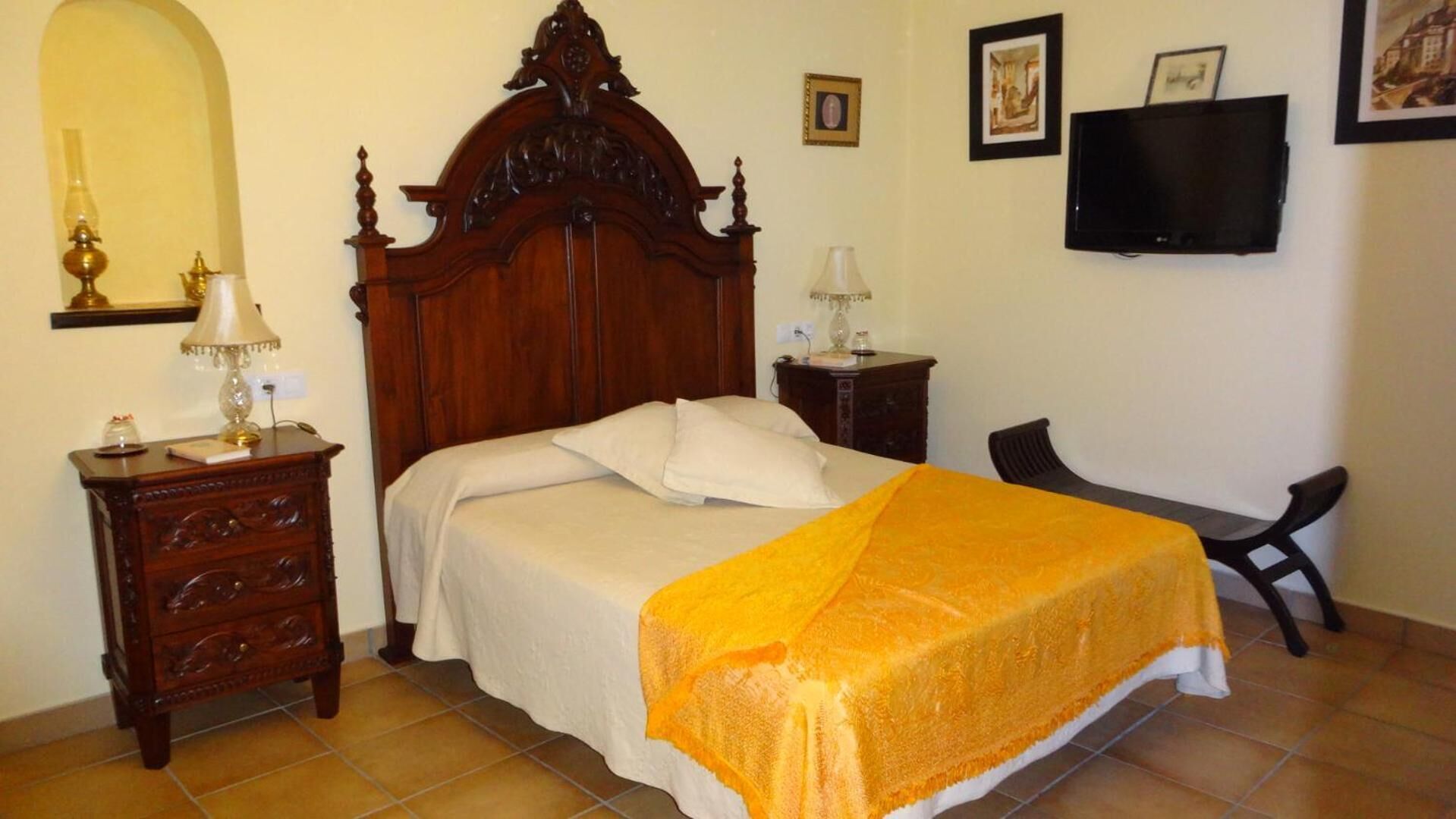 A bedroom with a wooden bed, a desk, a chair, a TV, and a lamp.