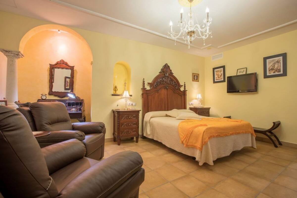 A bedroom with a bed, a sofa, a nightstand, a TV, and a chandelier.