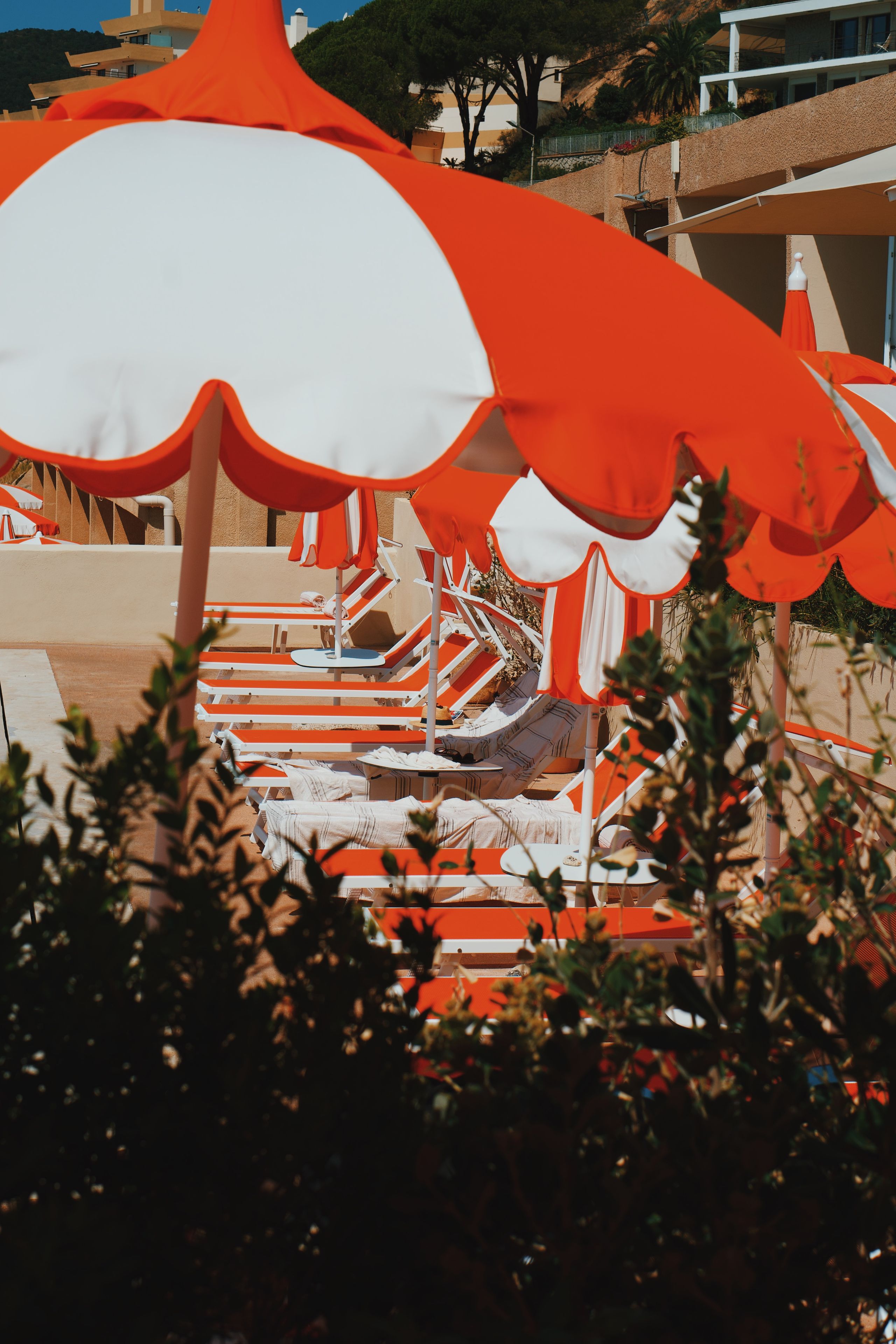 A row of sun loungers with orange and white striped cushions, arranged in a line with umbrellas overhead.