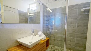 A modern bathroom with a glass-enclosed shower, a wooden vanity with a white sink, and a large mirror.