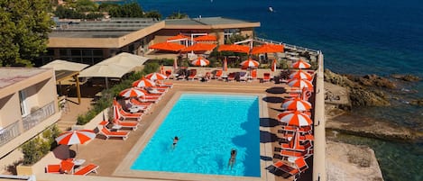 Una piscina con tumbonas y sombrillas, rodeada de edificios y vista al mar.