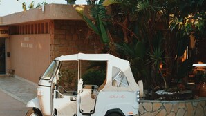 Un véhicule de golf blanc est garé devant un bâtiment à la façade en pierre, agrémenté de plantes tropicales.