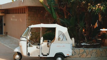 Un carrito de golf blanco estacionado frente a un edificio de fachada de piedra y plantas tropicales.