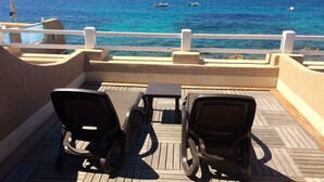 A deck with two chairs and a table, overlooking a calm sea with boats.