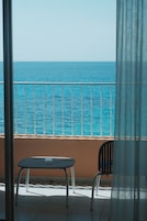 A balcony with a table and chairs, overlooking a calm sea.