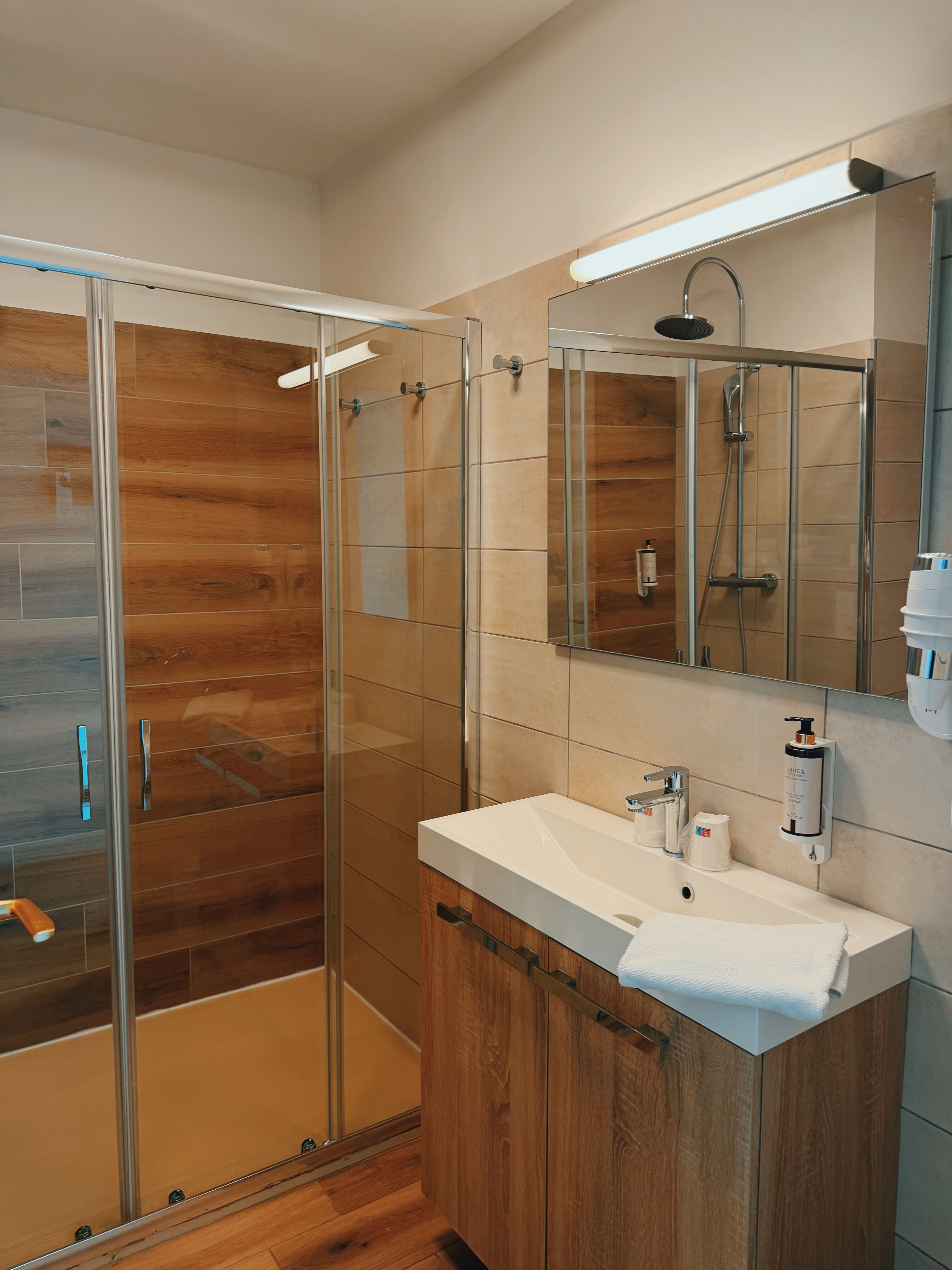 Un baño moderno con cabina de ducha de vidrio, tocador de madera y un espejo grande.