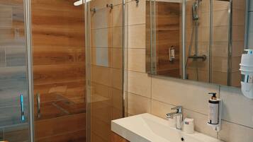 Un baño moderno con cabina de ducha de vidrio, tocador de madera y un espejo grande.