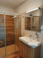 Un baño moderno con cabina de ducha de vidrio, tocador de madera y un espejo grande.