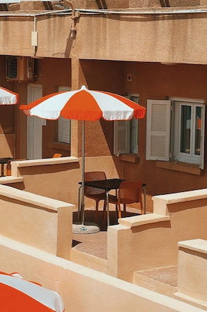 Une terrasse avec des sièges extérieurs, comprenant des chaises et des tables, ainsi qu’un espace couvert avec des parasols.