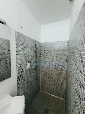 Ein modernes Badezimmer mit Mosaikfliesen, einer Dusche und einem weißen Waschbecken.