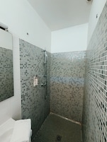 Un baño moderno con paredes de mosaico, una ducha y un lavamanos blanco.