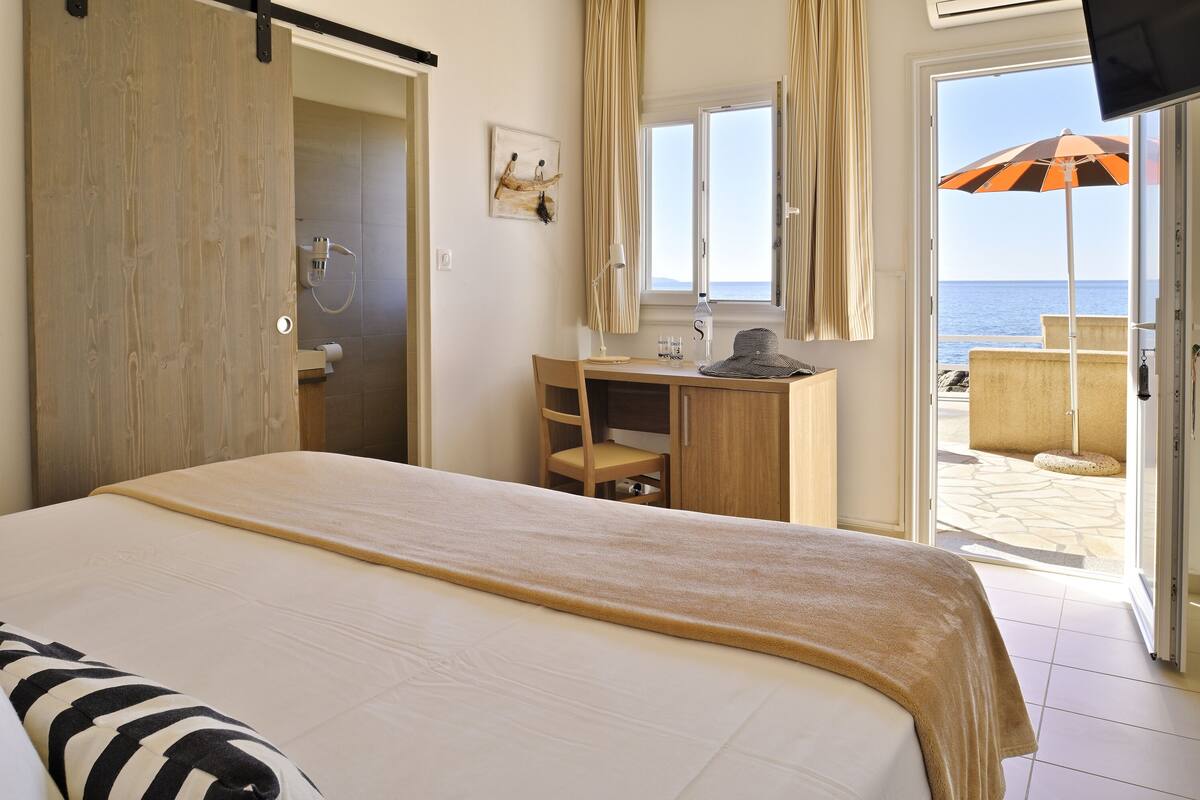 Une chambre d’hôtel avec un lit, un bureau, une chaise, une salle de bain et une vue sur la plage.