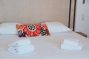 Una cama bien hecha con sábanas blancas, dos almohadas con un estampado floral colorido y dos toallas enrolladas sobre la cama.