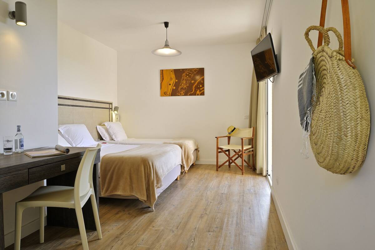 Une chambre d’hôtel équipée d’un lit, d’un bureau, d’une chaise, d’un téléviseur fixé au mur et d’un panier tressé suspendu au mur.