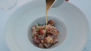 Un plato blanco con un plato de mariscos adornado con hierbas y especias, al que se le rocía una salsa.