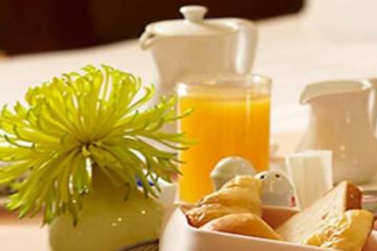 A breakfast tray with a pitcher of orange juice, a cup, a small bowl of fruit, and a covered silver tray.