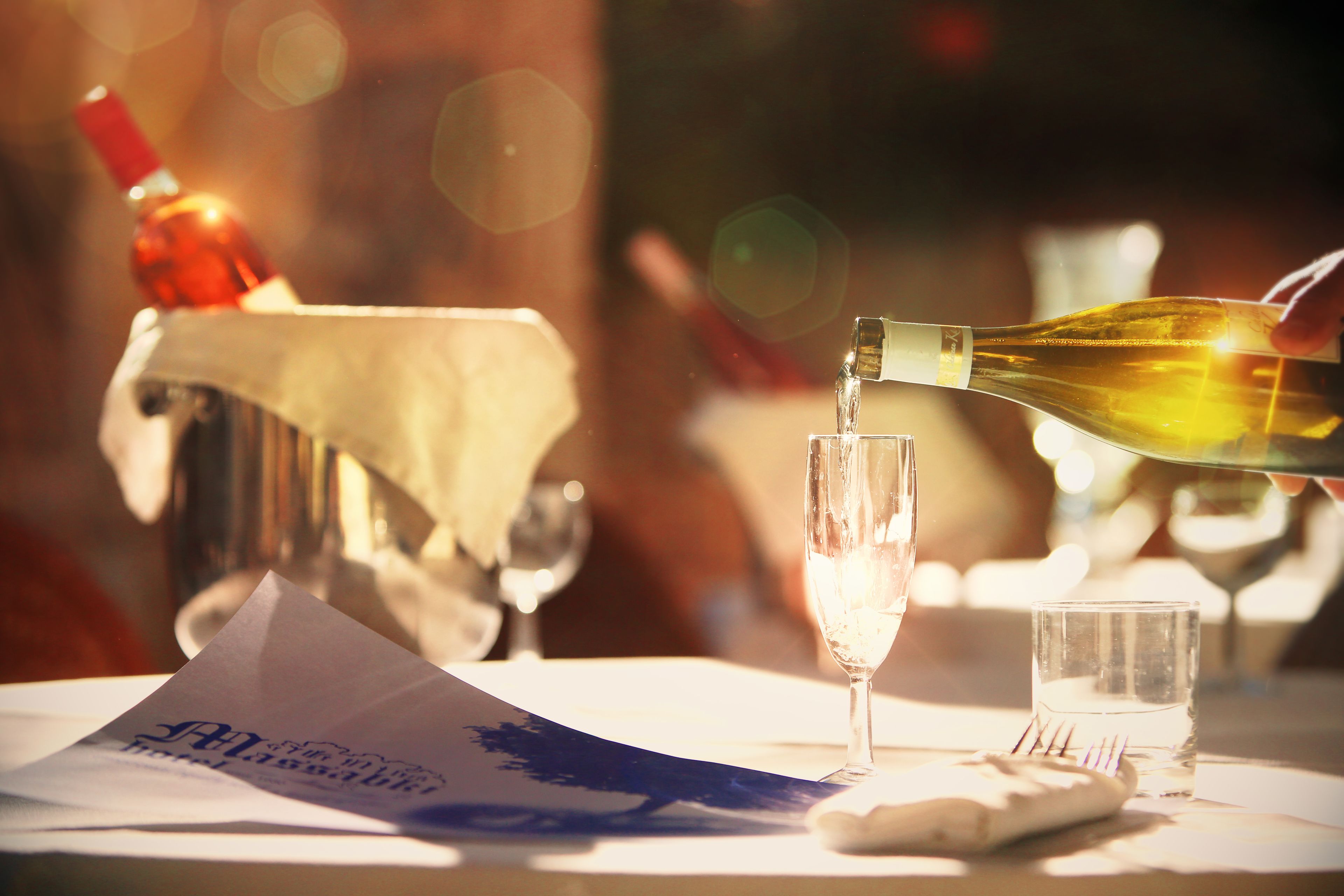 A bottle of champagne being poured into a glass, with a menu and a small glass of water on the table.