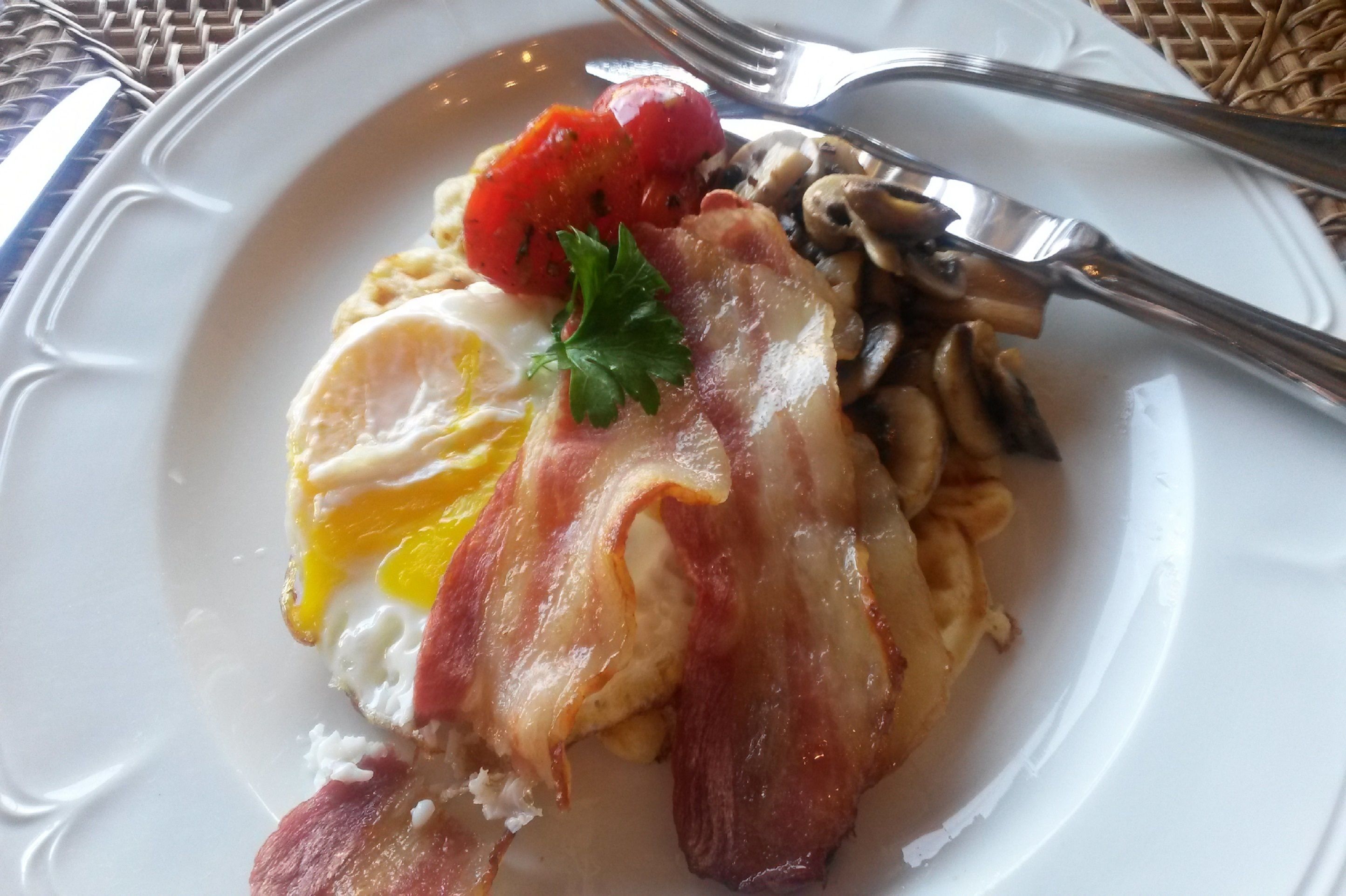 Un plato con huevos, tocino, champiñones y tomate.