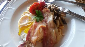 Un plato con huevos, tocino, champiñones y tomate.