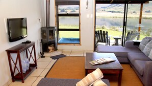Uma sala de estar com TV, lareira, sofá e vista para um lago.